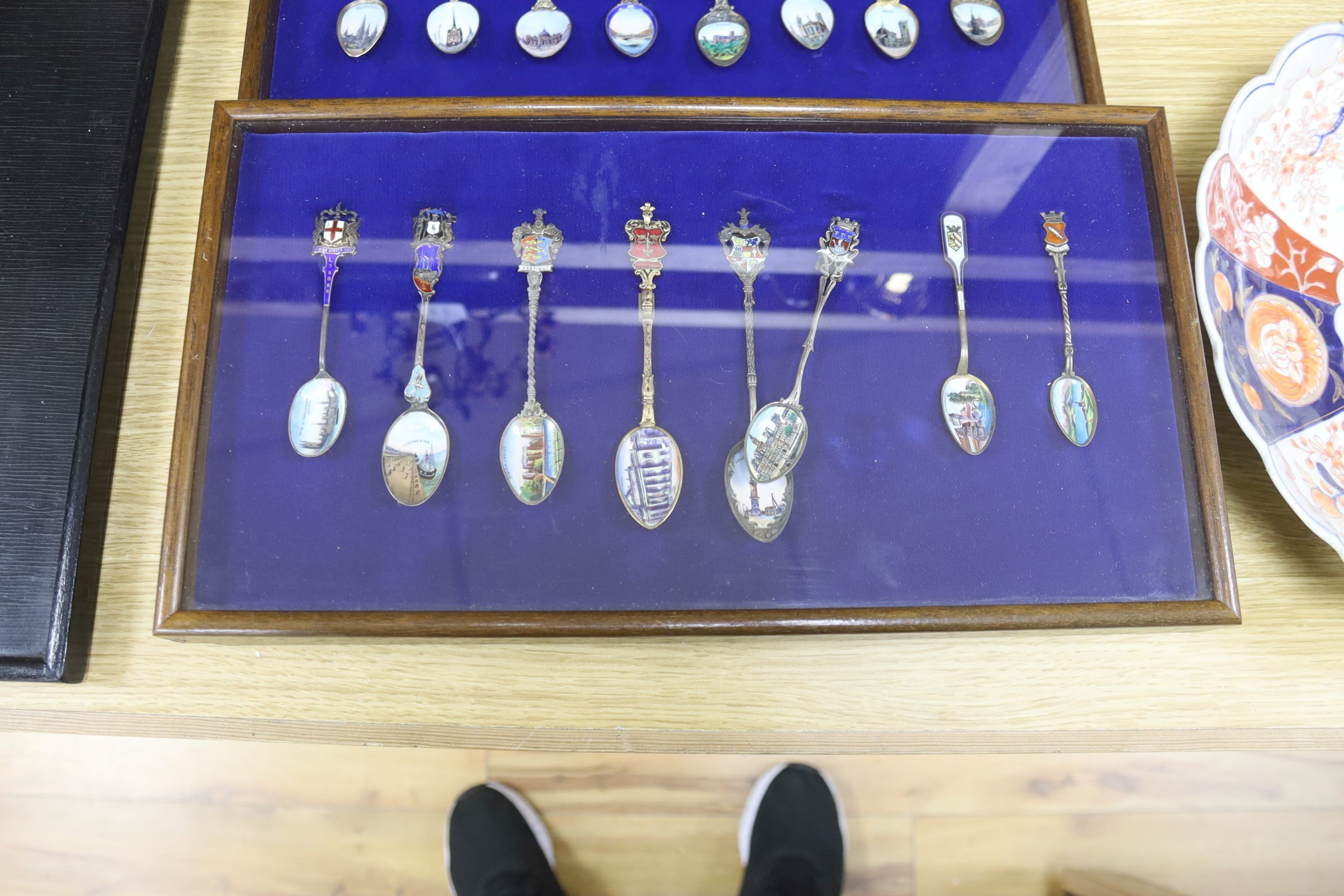 A collection of sixty four 800 standard silver (many gilt) and enamel souvenir spoons, early 20th century, in eight display cases, Including views of London, Germany, Italy, Austria, Spain etc.